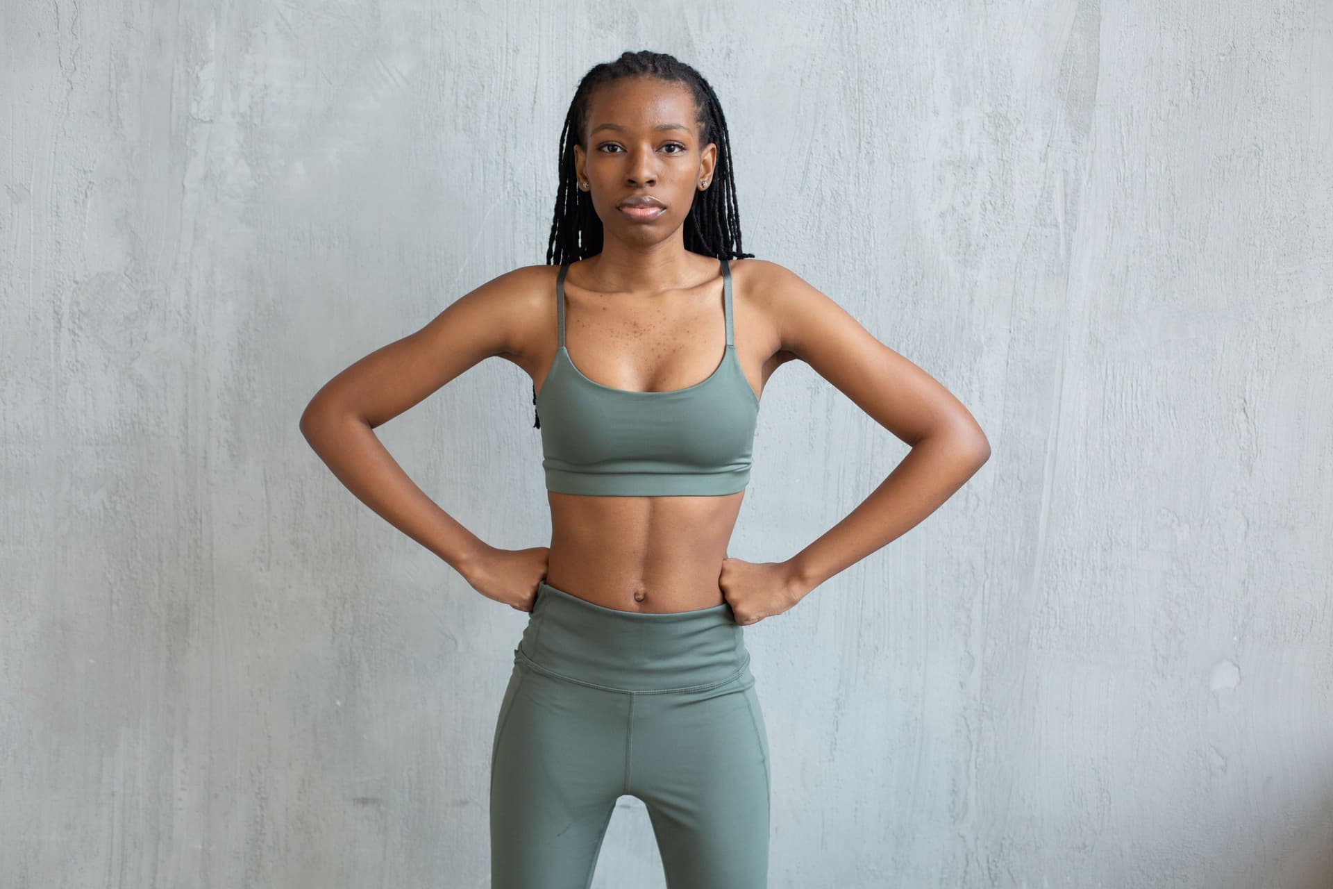 A person wearing dark leggings standing against a plain wall.