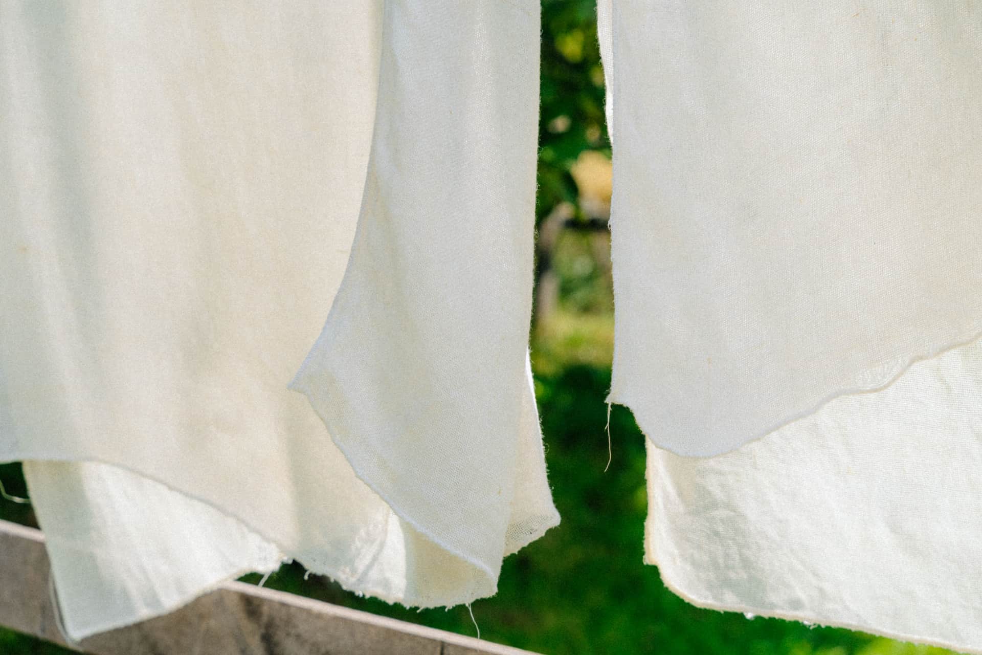 Light linen clothes hanging on a line outdoors.