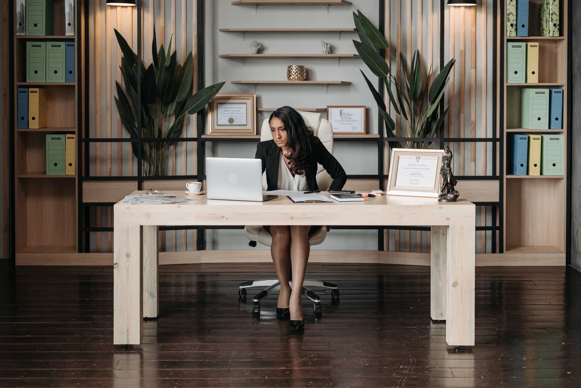 A person in a blazer seated at a desk in a neutral office.