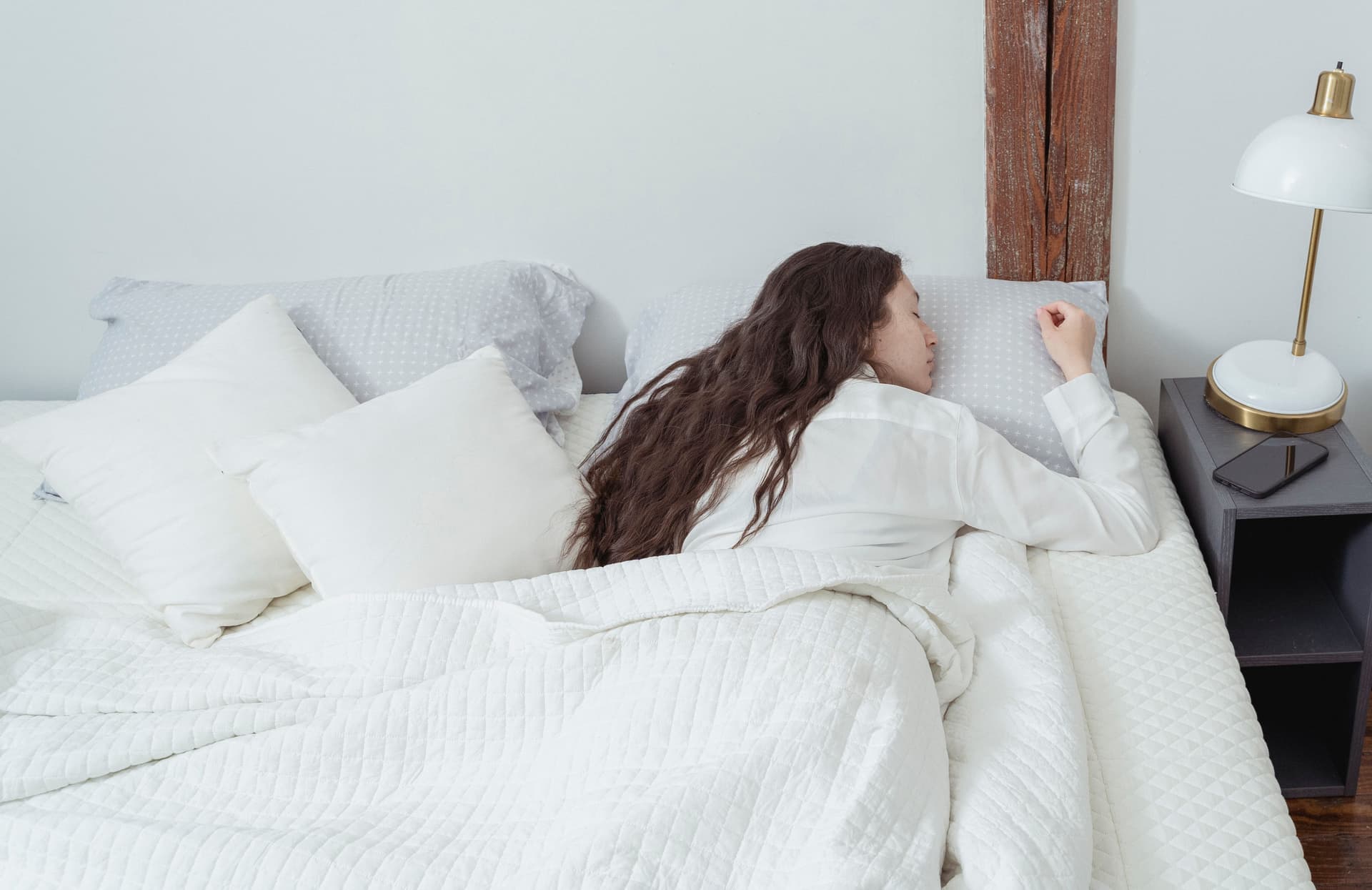 A person asleep on their side in bed with a pillow supporting their body, in soft daylight.