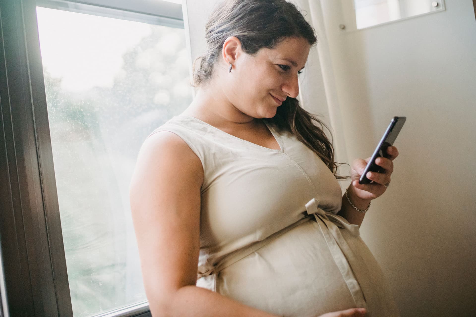 A pregnant person standing beside a window in calm natural light.