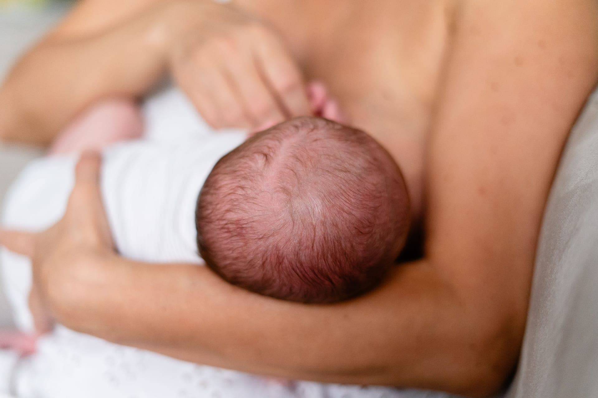 A parent feeding a newborn baby while seated in a quiet, neutral room.