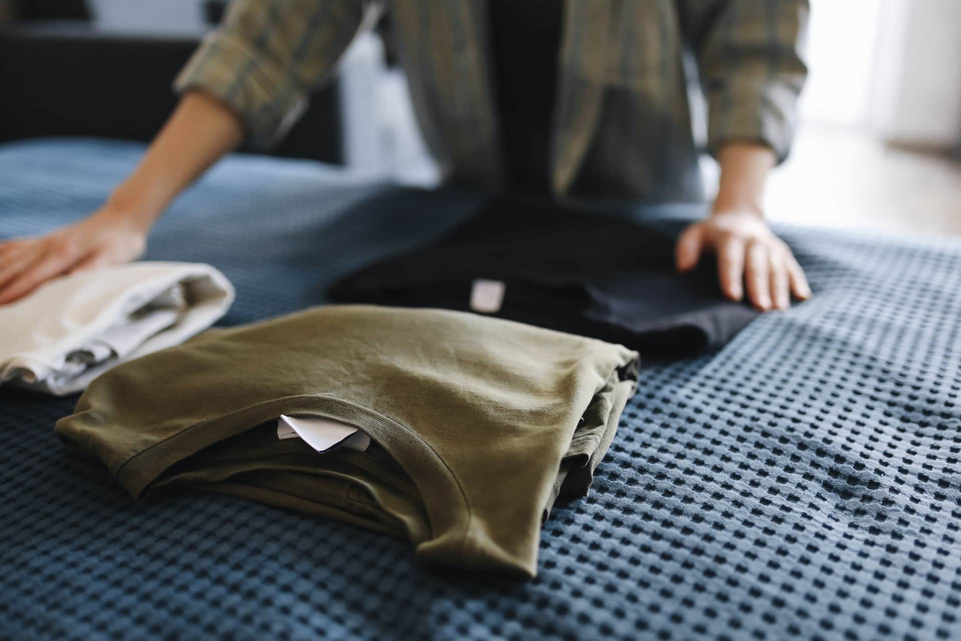 Soft folded clothes on a bed beside a lamp at night.