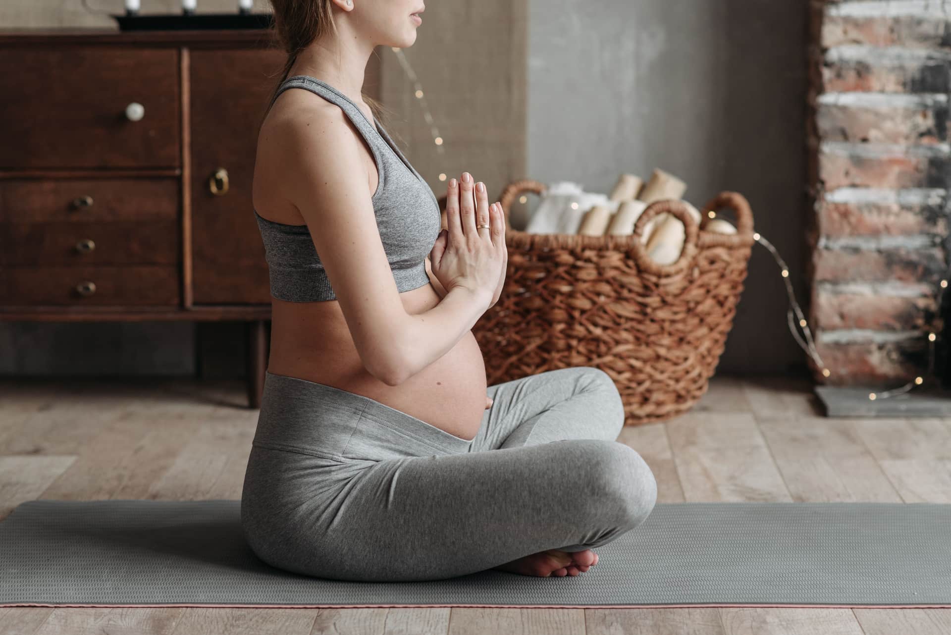 A pregnant person wearing leggings and a plain tee against a neutral wall.