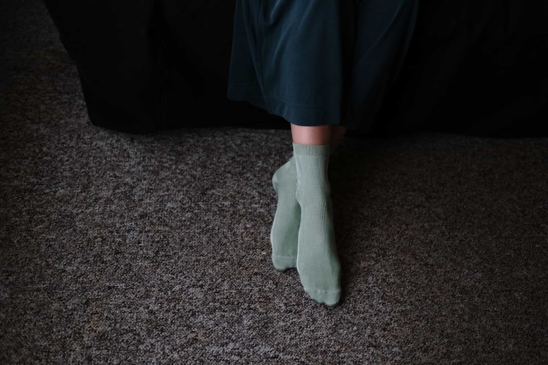 A person's legs in knee-high socks while seated on a sofa.