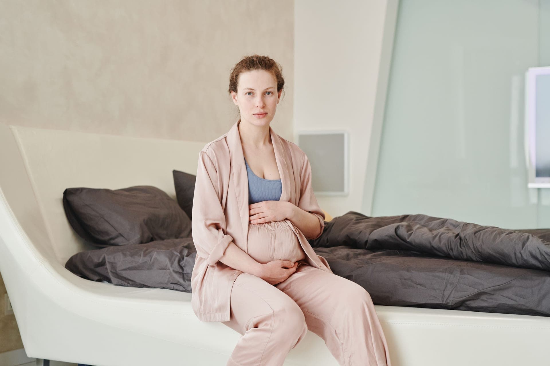 A person sitting on the edge of a bed holding their hip.
