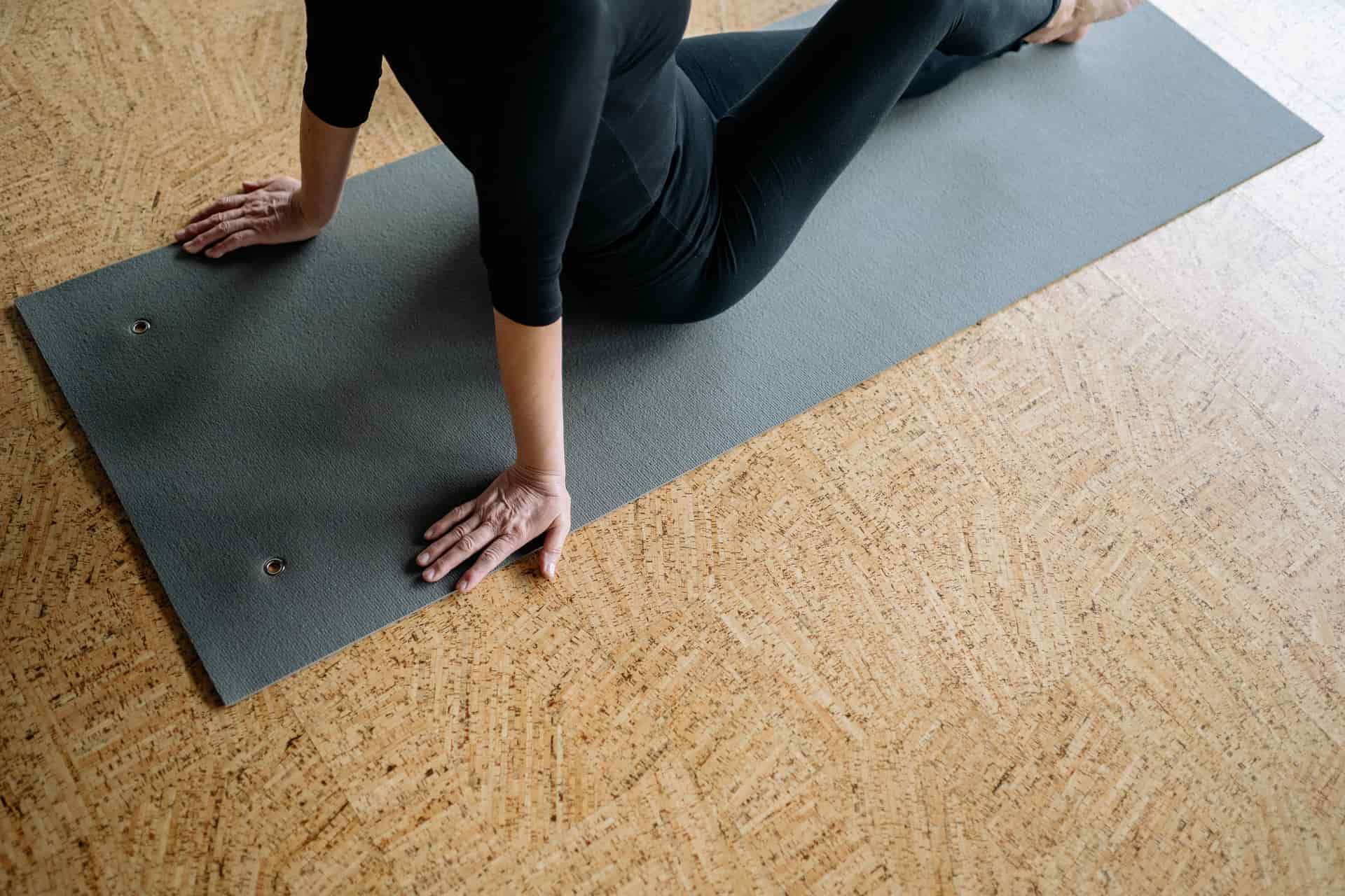 A person sitting on the floor stretching their hips on a neutral mat.