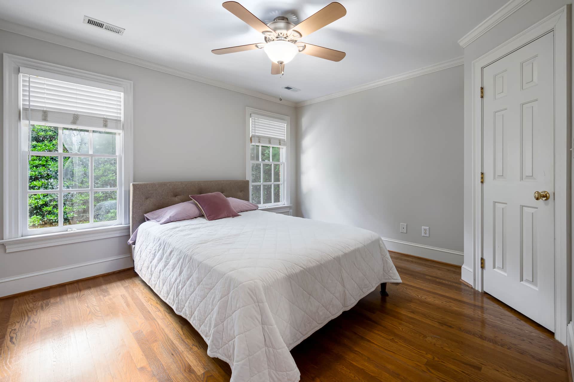 White linen bedding beside an open window in a bright bedroom.