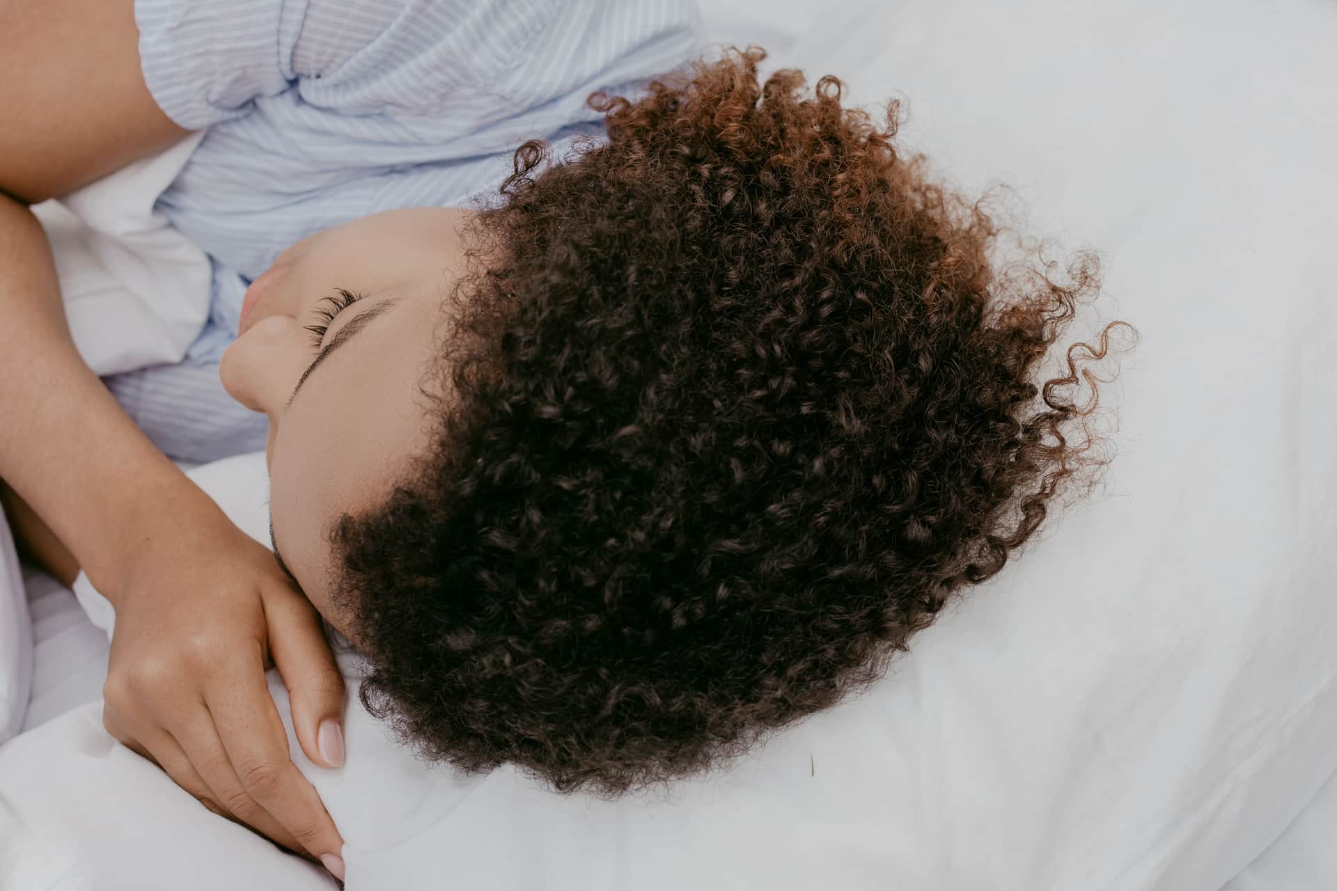 A person lying on their side in bed with a pillow between their knees.
