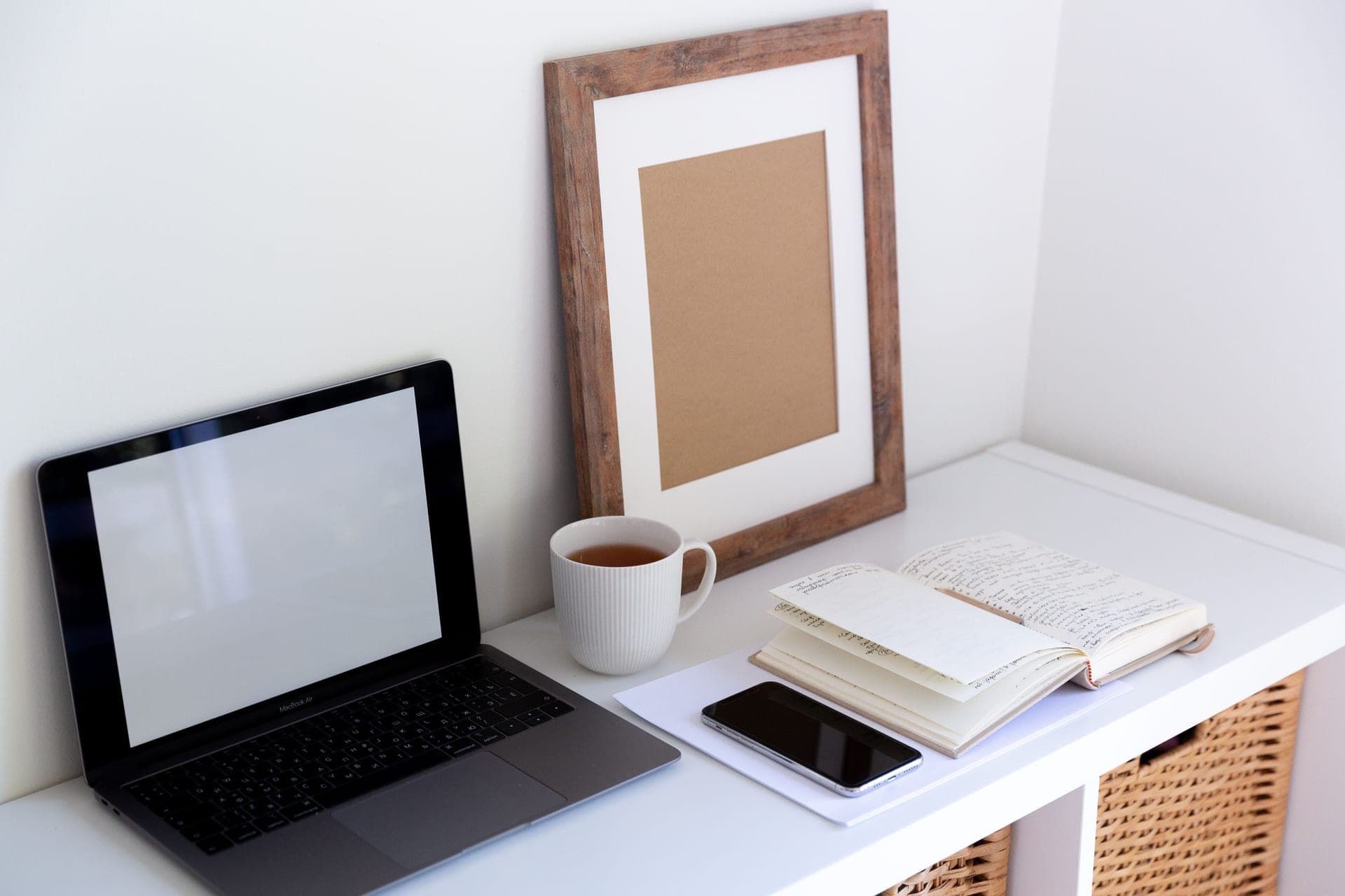 A desk with a laptop, an open notebook and a cup of tea.